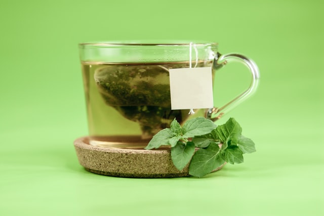 a cup of green tea with peppermint leaves sitting on a cork coaster