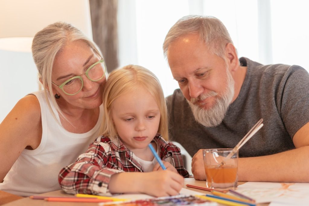 grandparents watching over their young granddaughter and teaching her to draw