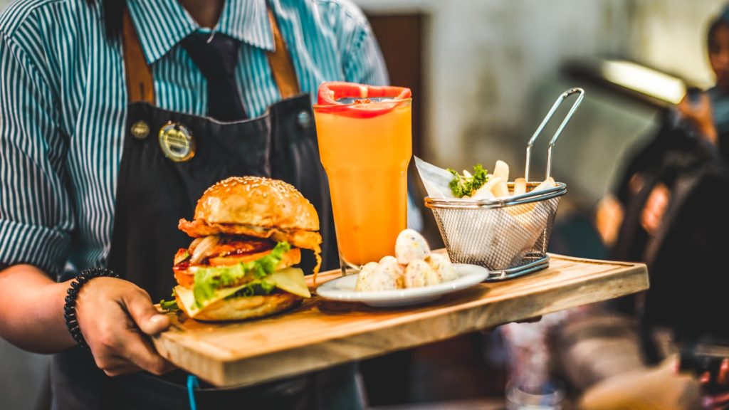 server carrying wooden tray with burger, fries, and beer