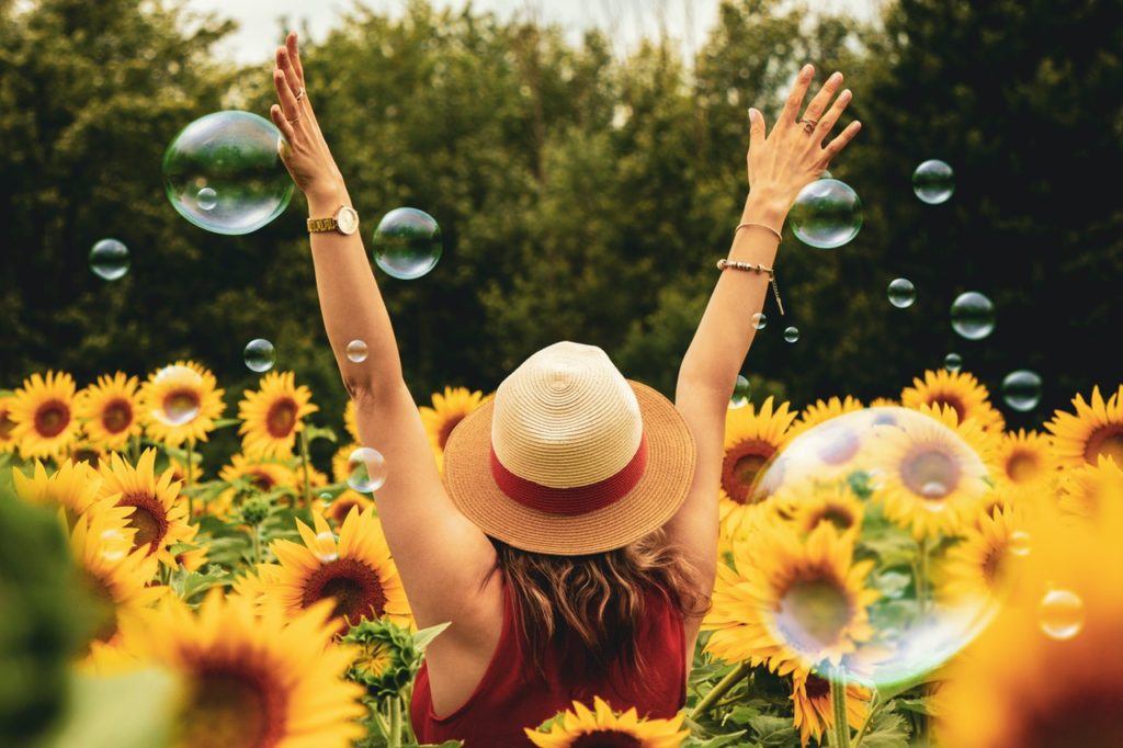 woman facing forward in the middle of a sunflower field with soap bubbles around
