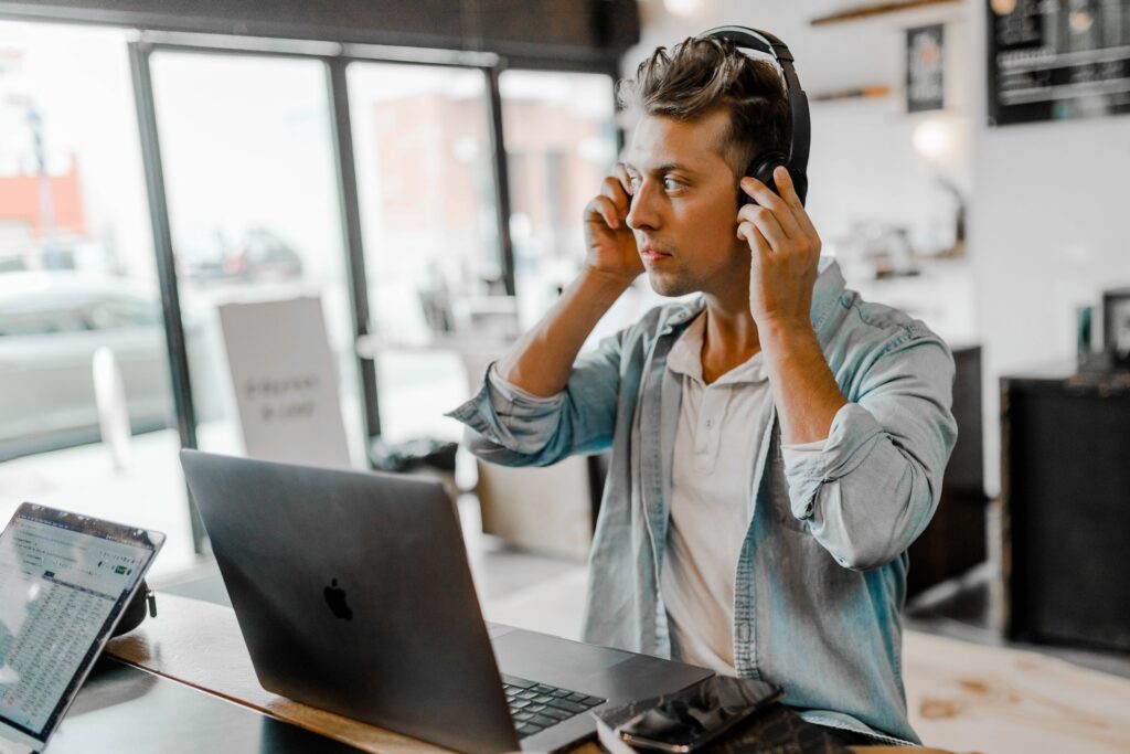 man putting on his headset and working on his macbook in a coworking office space