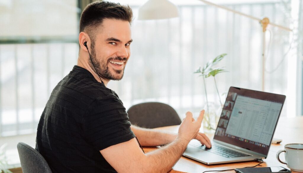 smiling man working remotely at home on his laptop while on a video conference call with team