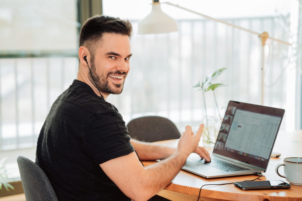 smiling man working remotely at home on his laptop while on a video conference call with team