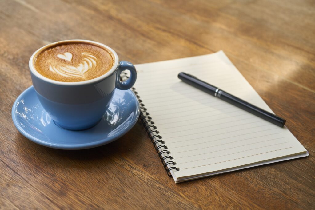 A latte in a blue mug next to a notepad