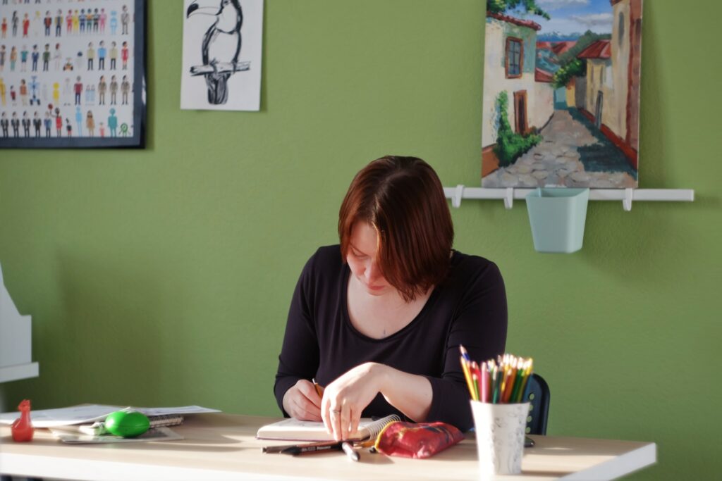 A woman sitting and working at a desk in front of a green wall