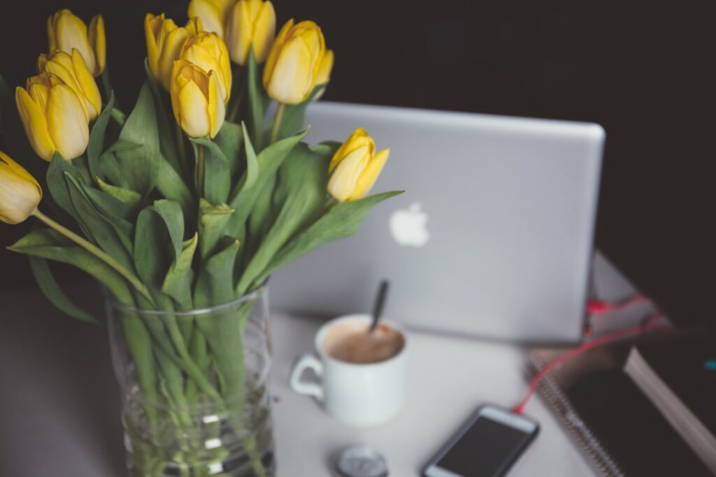 Yellow tulips on a desk with a laptop, phone, and coffee mug